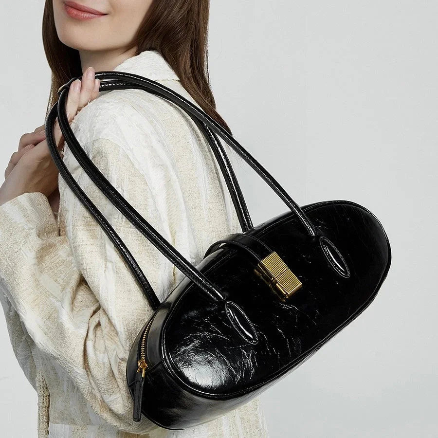 Woman wearing white sweater holding black patent leather oval shoulder bag with gold clasp