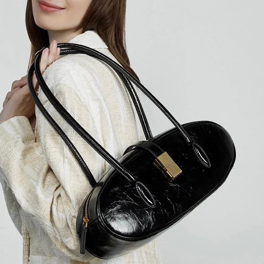 Woman wearing white sweater holding black patent leather oval shoulder bag with gold clasp