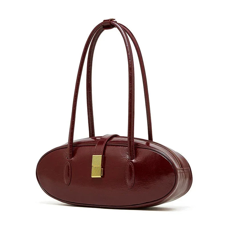 Oval-shaped burgundy leather handbag with gold clasp and double handles on white background