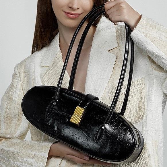 Woman holding black leather handbag with gold clasp, wearing textured white blazer