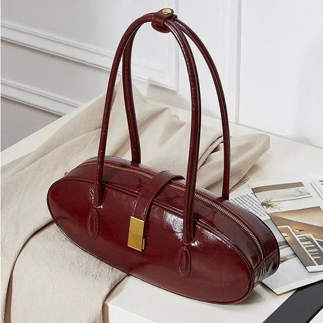Glossy burgundy leather handbag with double handles on cream fabric, modern setting
