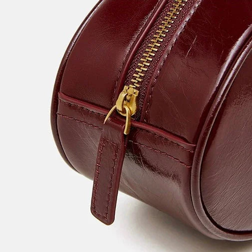 Close-up of burgundy leather round handbag with gold zipper on white background