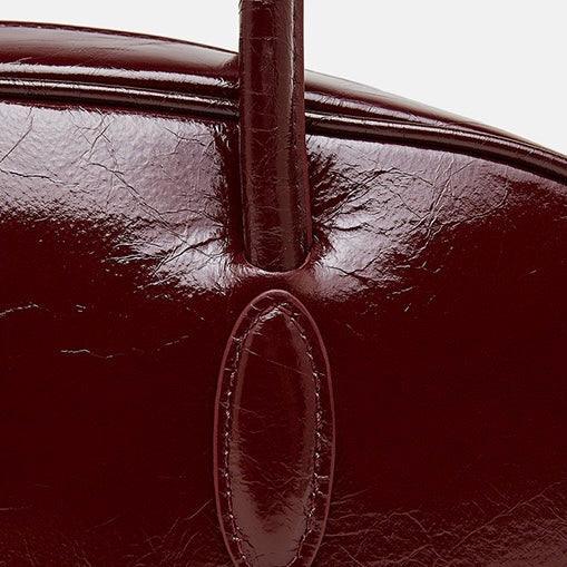 Close-up of glossy dark red leather handbag handle and stitching detail