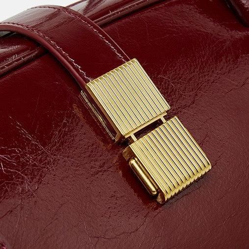 Close-up of burgundy leather handbag with gold metal clasp and glossy finish
