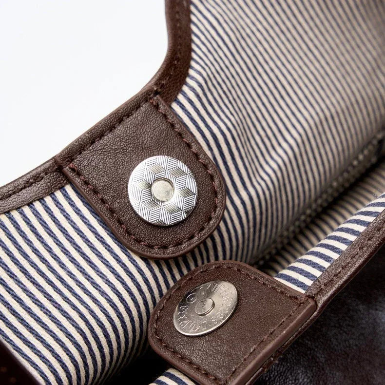 Striped fabric bag with brown leather trim and metallic snap buttons, close-up view.