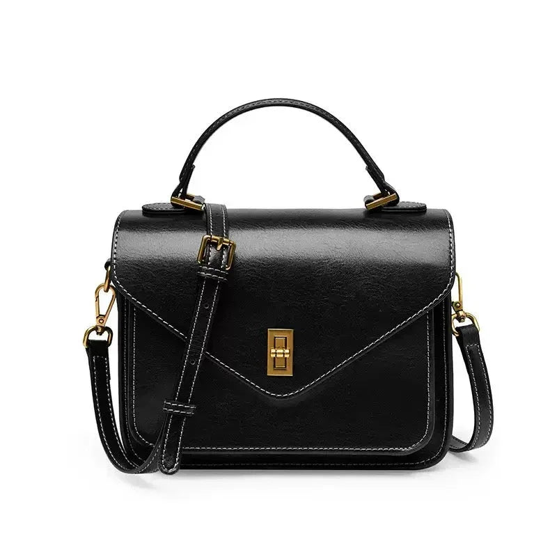 Black leather crossbody handbag with gold hardware and top handle on white background