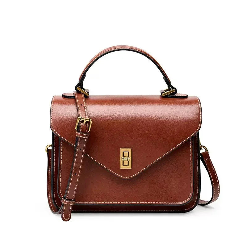 Brown leather crossbody handbag with gold buckle and top handle on white background