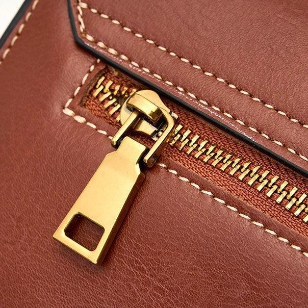 Close-up of a gold zipper on a brown leather bag with white stitching detail