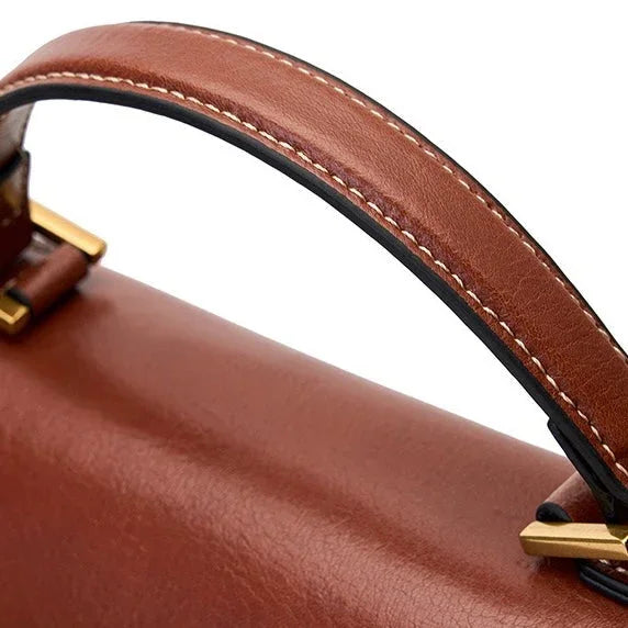 Close-up of brown leather handbag handle with gold hardware and white stitching