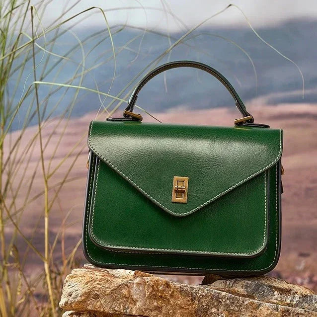 Green leather handbag with top handle on rocks outdoors, nature background