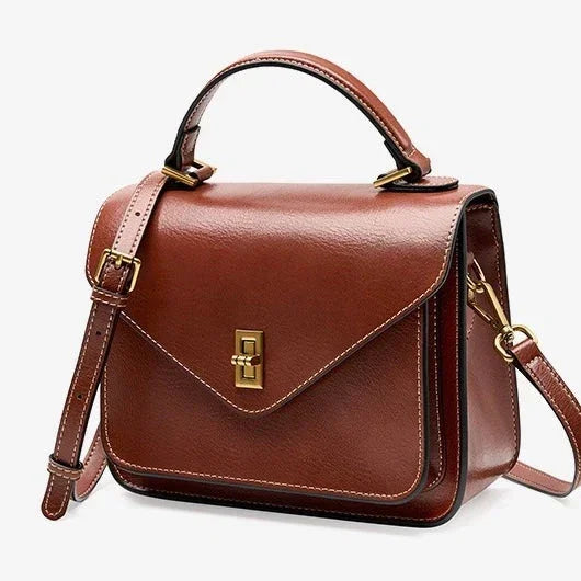 Brown leather crossbody satchel bag with gold hardware and top handle on white background