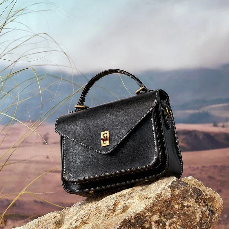 Black leather handbag with gold clasp on rock in outdoor landscape with hills