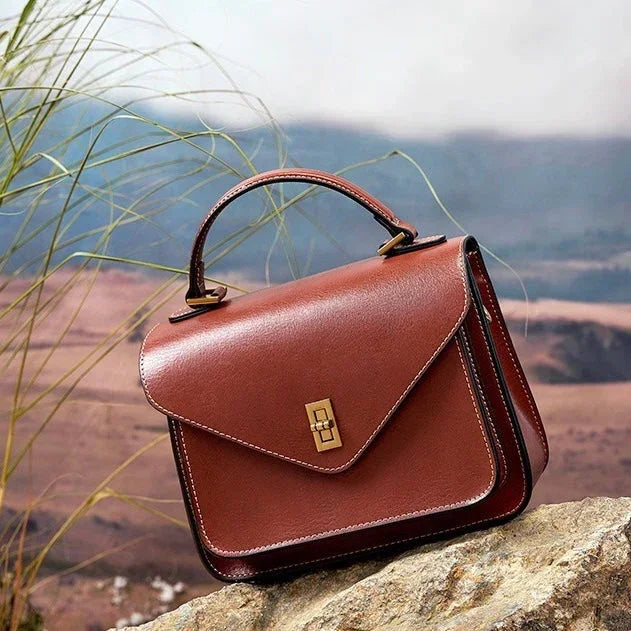 Brown leather handbag with gold clasp on rock, mountain landscape background