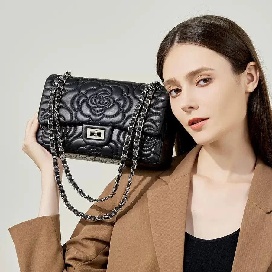 Woman holding a black quilted floral leather handbag with chain strap