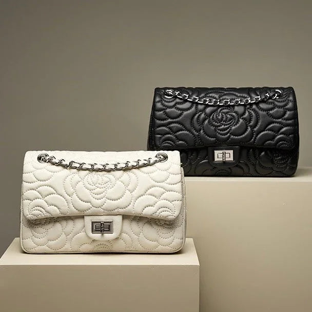Black and white quilted leather handbags with floral pattern and chain straps on beige pedestals