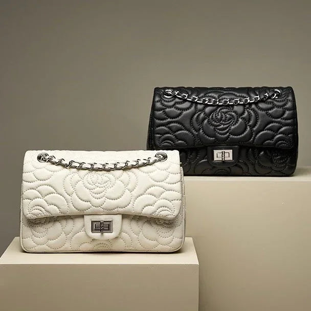 Black and white quilted leather handbags with floral pattern and chain straps on beige pedestals