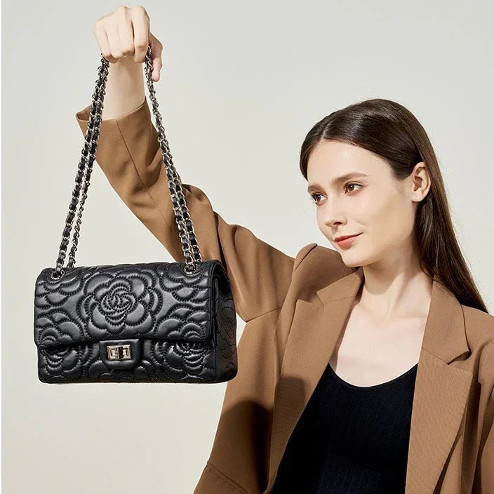 Woman holding black quilted leather handbag with floral pattern and chain strap