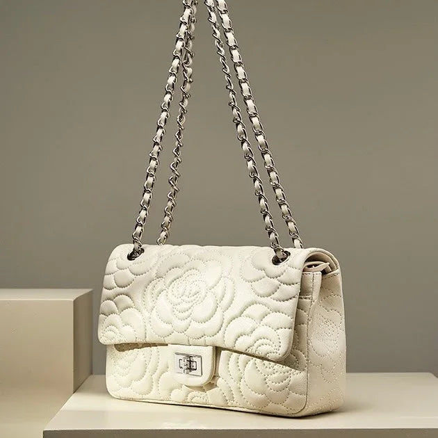 White quilted leather handbag with floral pattern and chain strap on beige display
