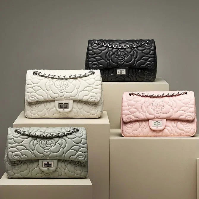 Four quilted floral leather handbags in black, white, pink, and gray on display pedestals