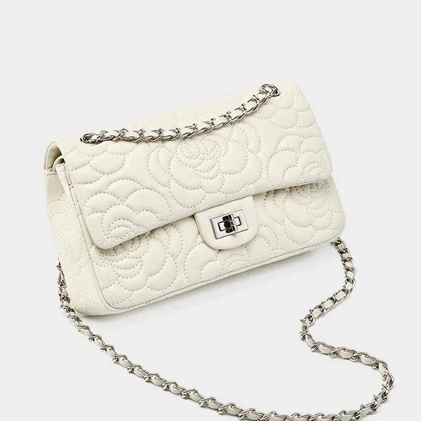 White quilted leather shoulder bag with floral pattern and silver chain strap on white background