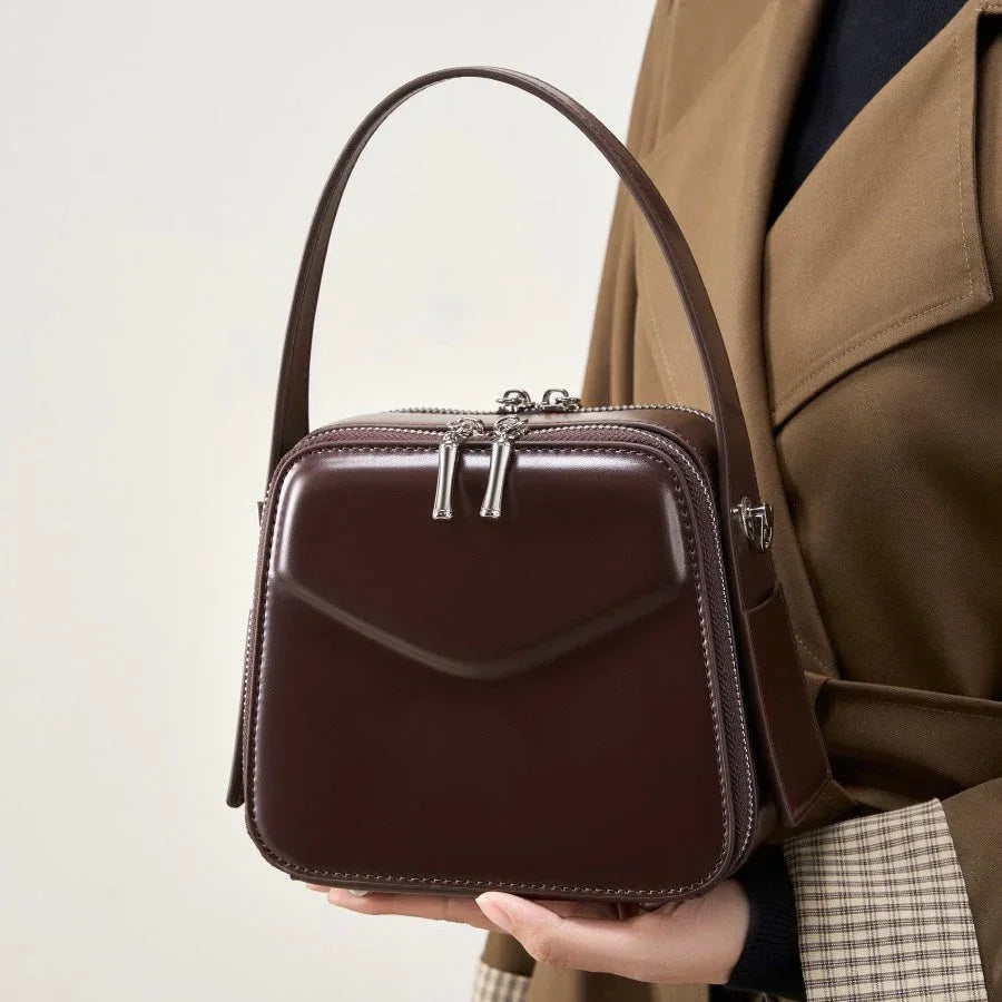 Woman holding a brown leather box handbag with silver zippers and top handle