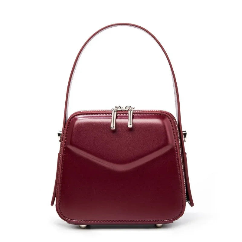 Burgundy leather handbag with structured shape and top handle on white background