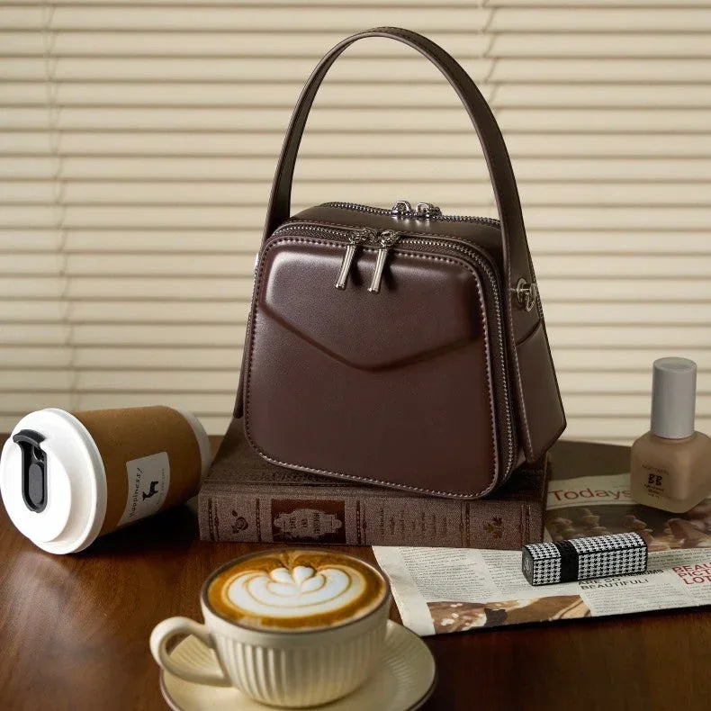 Brown leather handbag on books with coffee, lipstick, nail polish, and blinds background