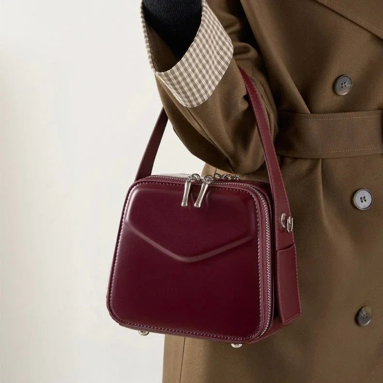 Woman holding burgundy leather square handbag, brown coat background, fashion accessory