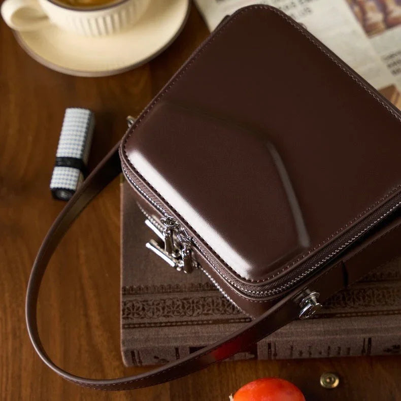 Glossy brown leather crossbody bag on table with coffee and newspaper, elegant accessory