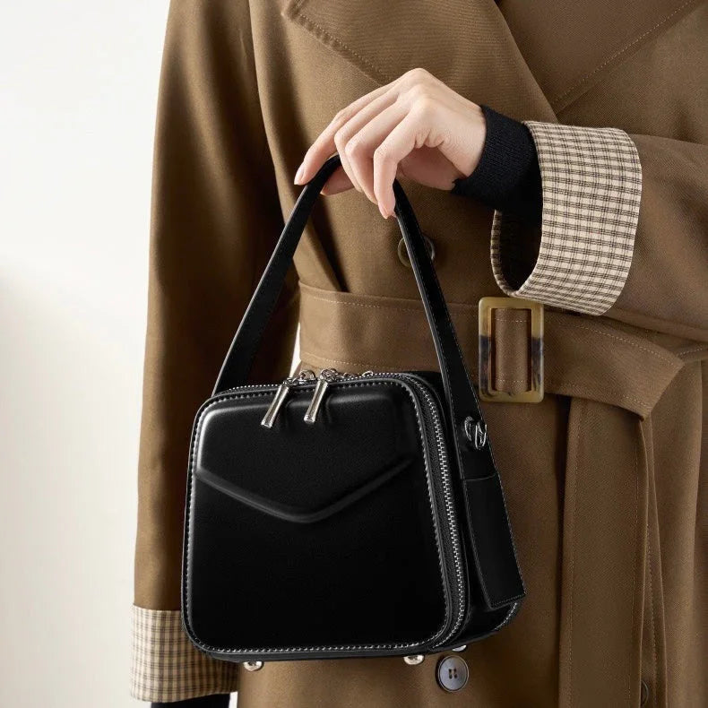 Woman in brown trench coat holding a black leather handbag with zipper details