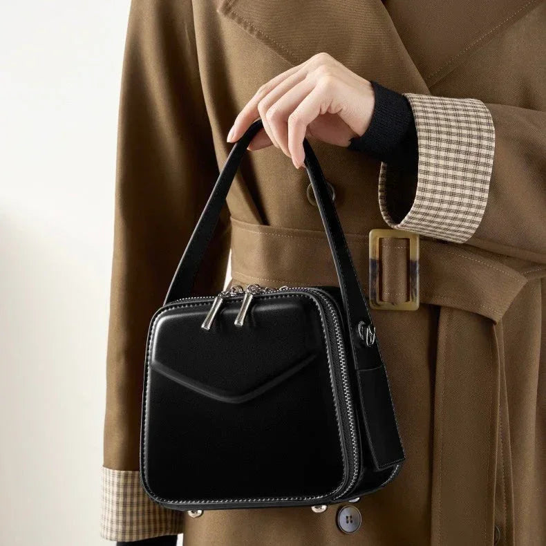 Woman in brown trench coat holding a black leather handbag with zipper details