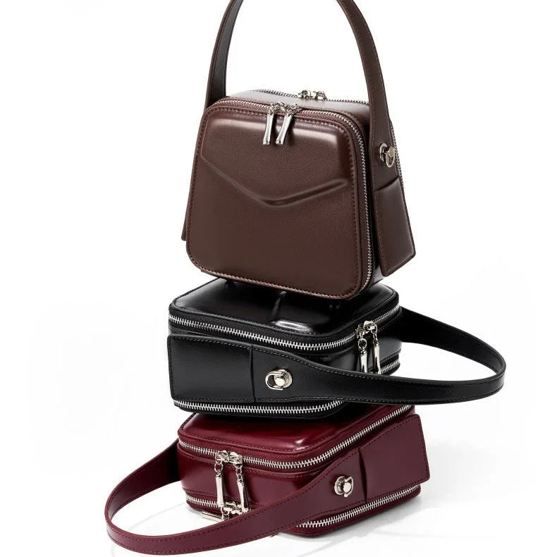 Stack of three square leather handbags in brown, black, and burgundy with zippers and handles