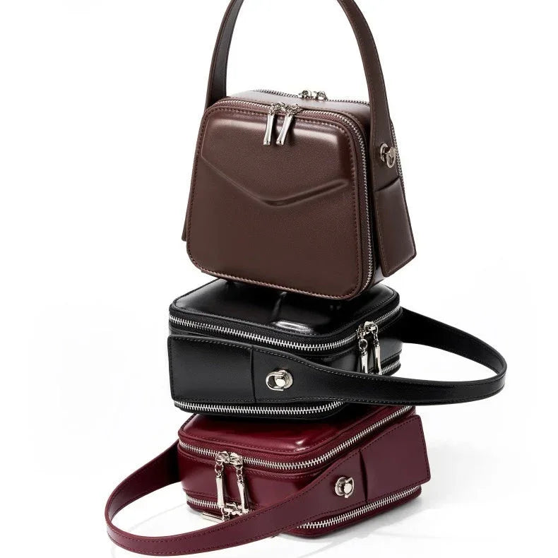 Stack of three square leather handbags in brown, black, and burgundy with zippers and handles
