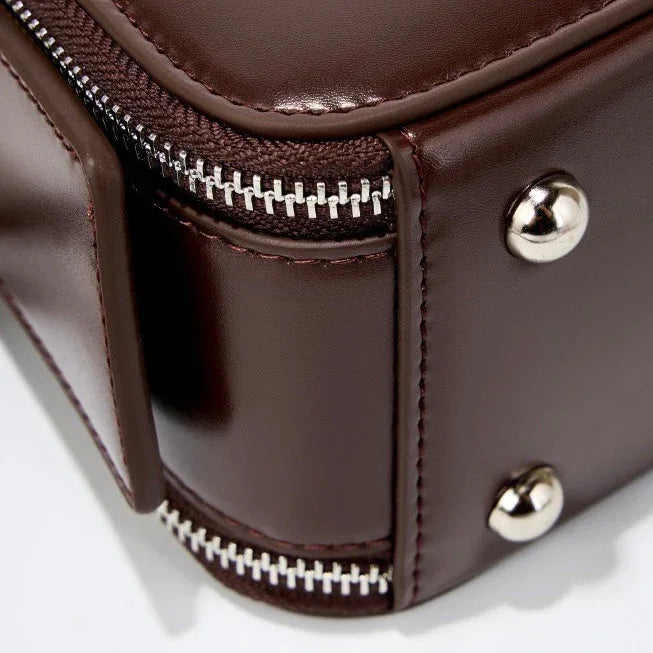 Close-up of brown leather bag corner with metal studs and silver zipper detail