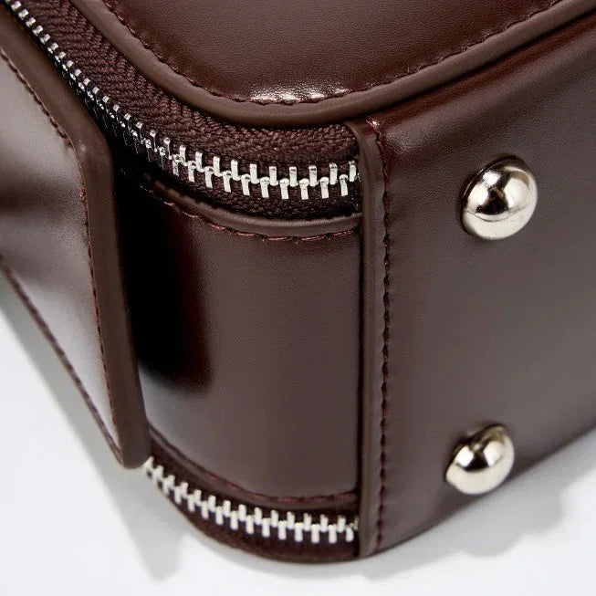 Close-up of brown leather bag corner with metal studs and silver zipper detail