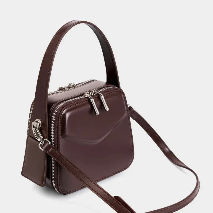 Brown leather square crossbody bag with top handle and silver zippers on white background