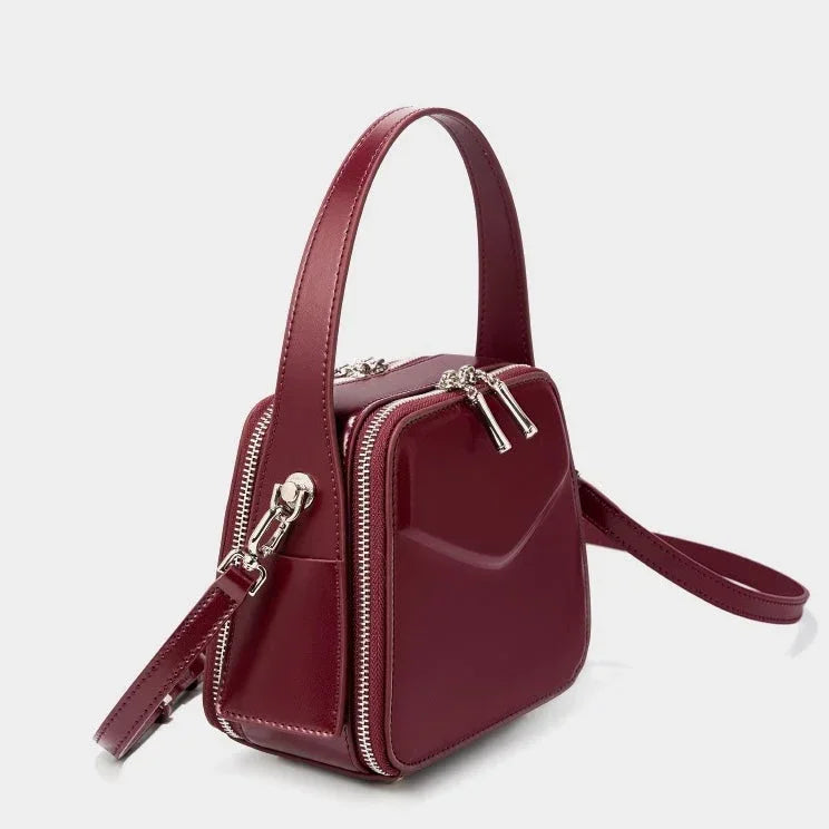 Burgundy square leather handbag with top handle, silver zippers, and crossbody strap