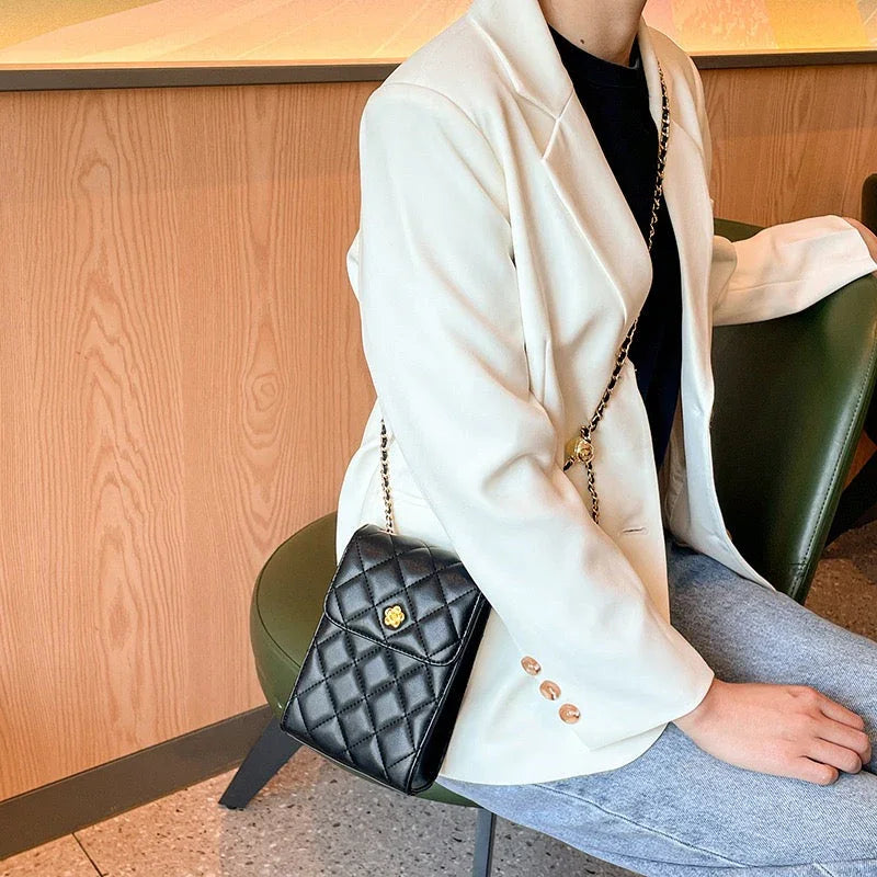 Woman in white blazer with black quilted crossbody bag sitting on green chair