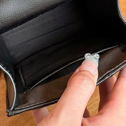 Hand holding open a black leather wallet on a wooden surface