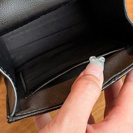 Hand holding open a black leather wallet on a wooden surface
