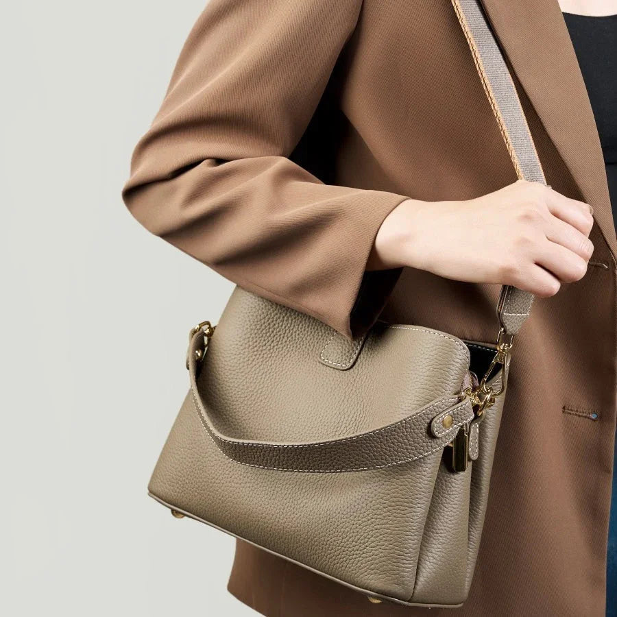 Woman in brown blazer carrying taupe leather shoulder bag with gold hardware