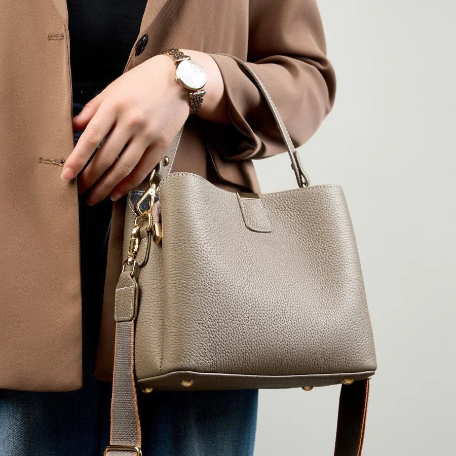Woman in brown blazer holding taupe leather handbag with gold hardware