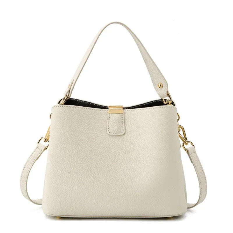 Beige leather handbag with gold hardware and detachable shoulder strap on white background
