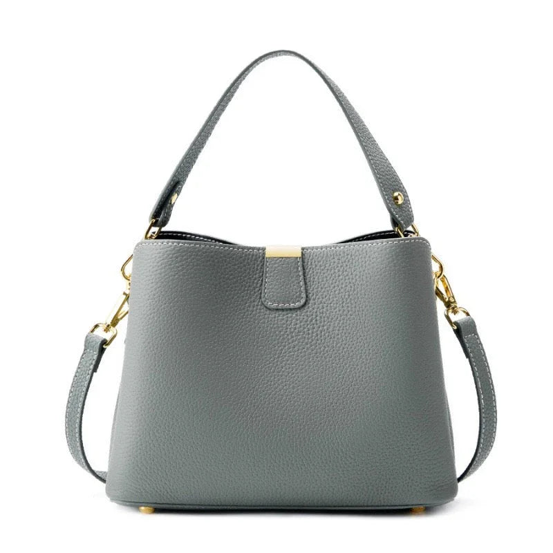 Gray leather handbag with gold hardware and detachable shoulder strap on white background