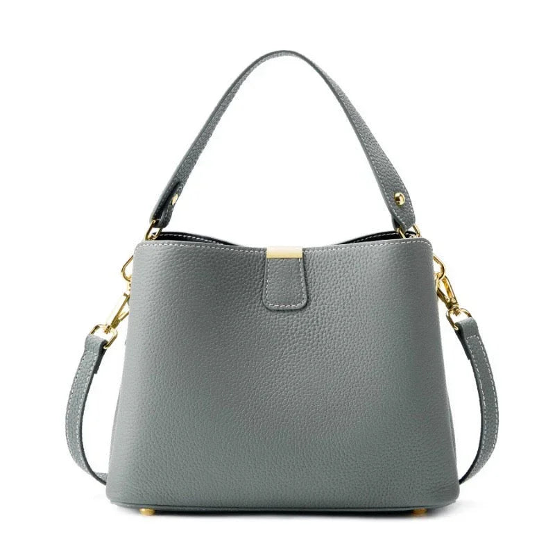 Gray leather handbag with gold hardware and detachable shoulder strap on white background