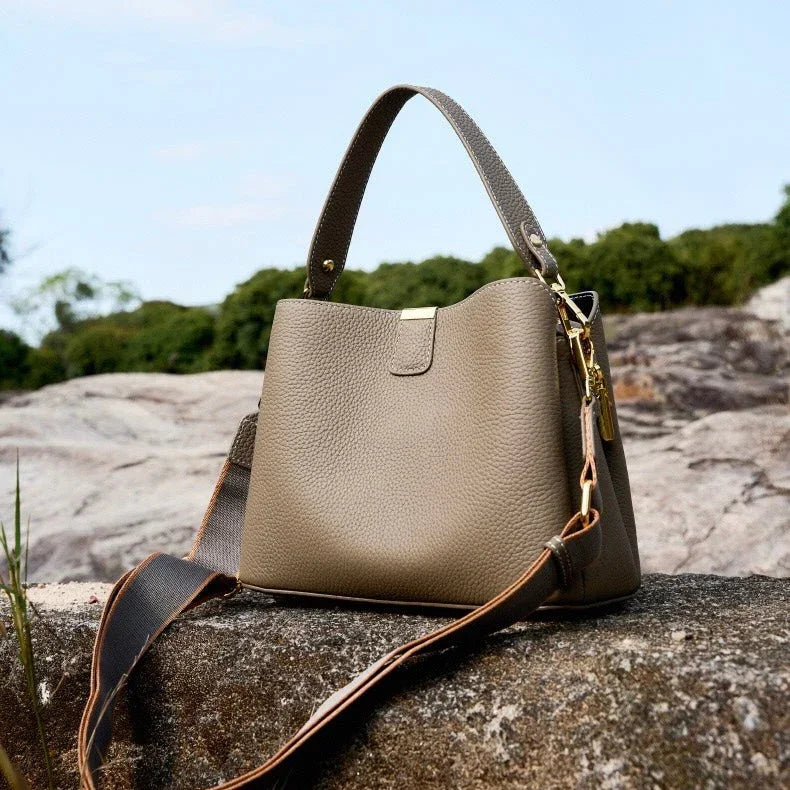 Taupe leather handbag with gold hardware on a rock outdoors, luxury fashion accessory