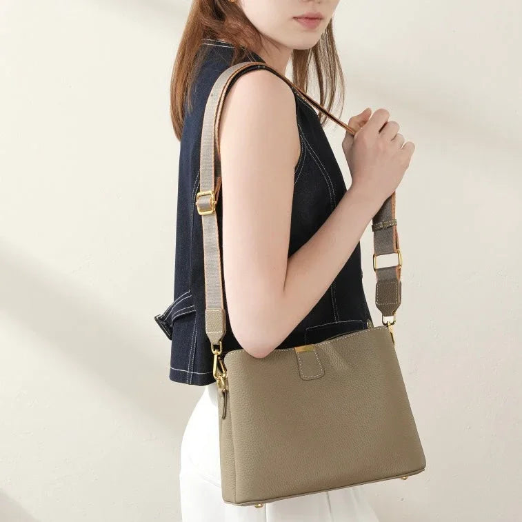 Woman wearing a taupe leather shoulder bag with gold hardware and wide strap