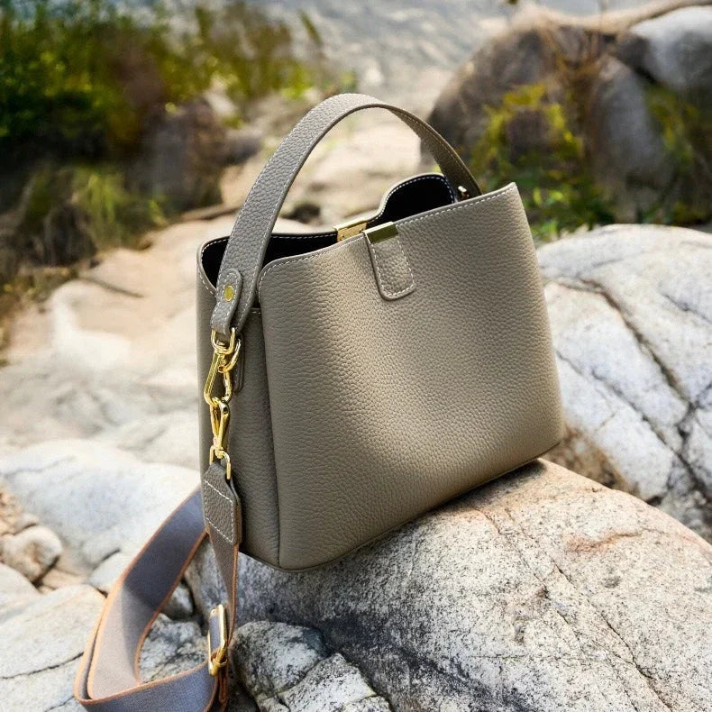 Taupe leather handbag with gold hardware on rocks outdoors
