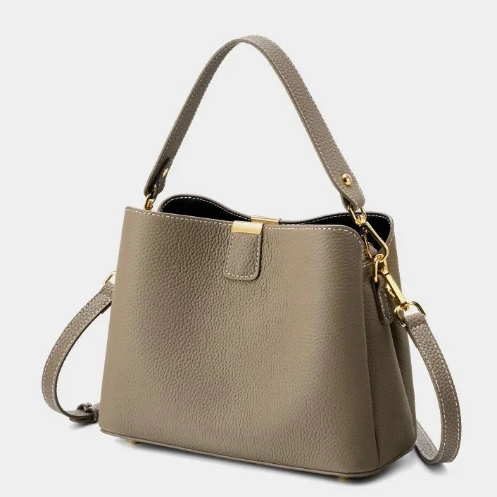 Taupe leather handbag with gold hardware and detachable shoulder strap on white background