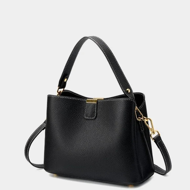 Black leather handbag with gold hardware, top handle and crossbody strap on white background